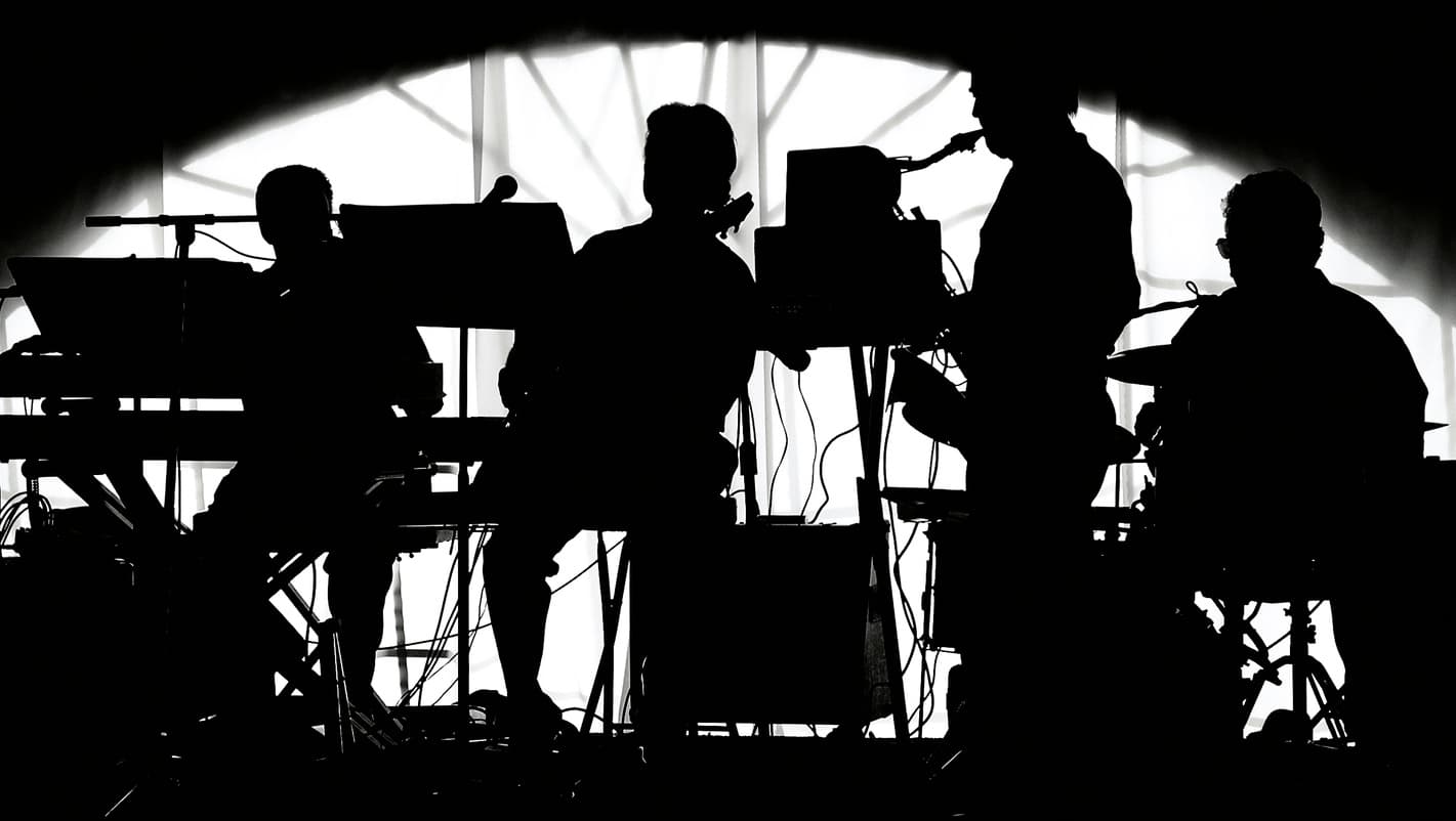 A five-piece band silhouetted during a live performance